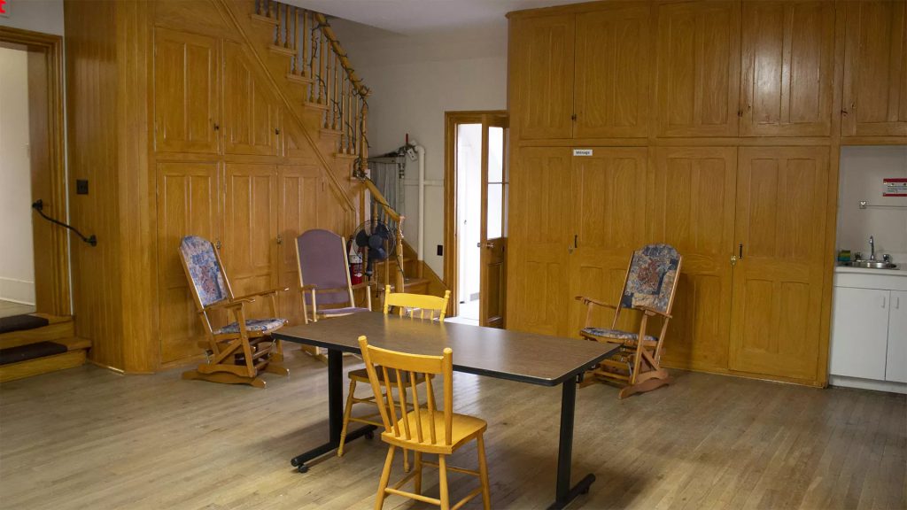 Grande salle meublée de chaises, d’une table et de grands placards en bois.